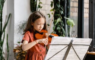 A young female child practicing her violin in a greenery-filled room
