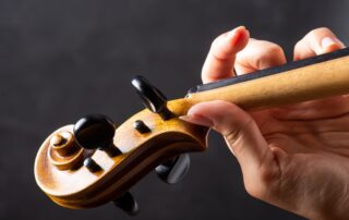 a violin headstock and a hand fingering the strings