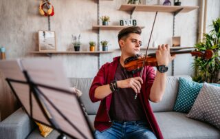 a man practicing violin in his living room sitting on a couch