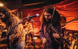 Group of men, musicians performing on stage together, including a man with an electric violin