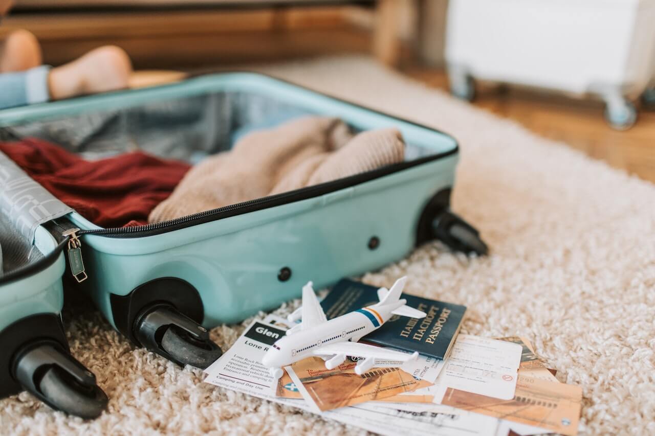 Open teal green suitcase with clothes, passport and travel documents strewn about