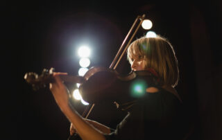 a woman playing a violin with stadium lights in the background