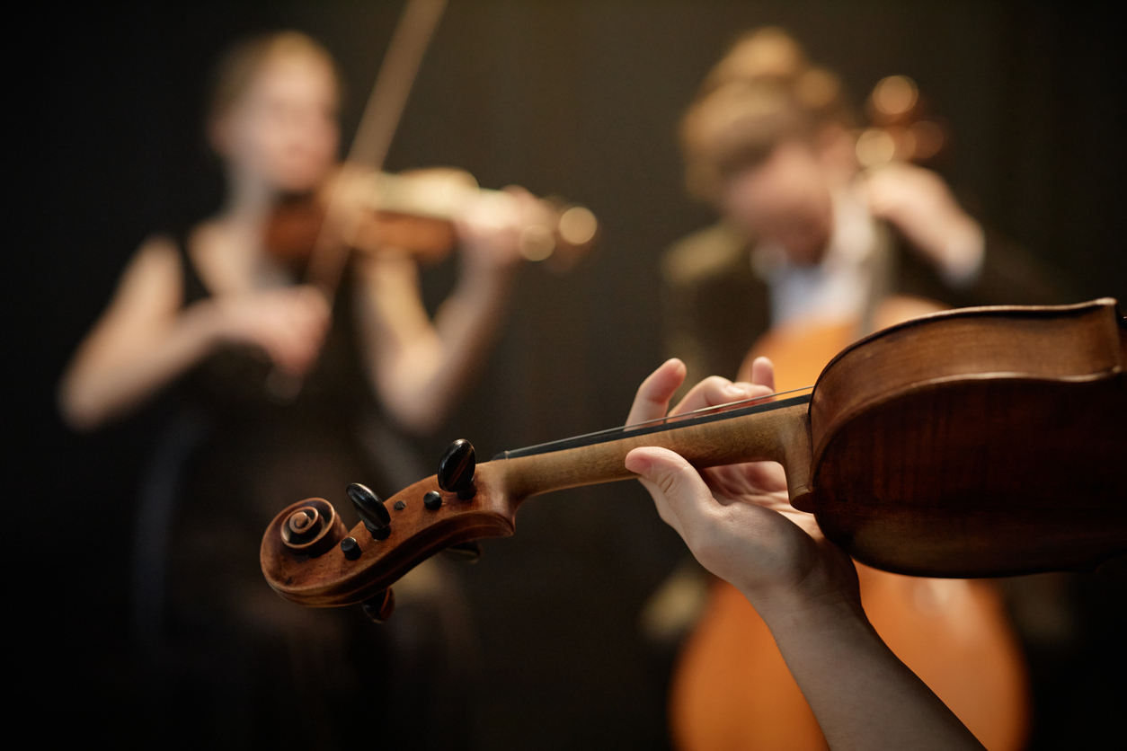Close up on hand of string ensemble musician playing on violin moving fingers on fretboard on blurred background with focus on hand