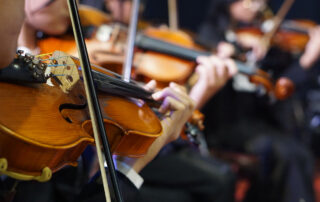close up of hands playing violin in orchestra