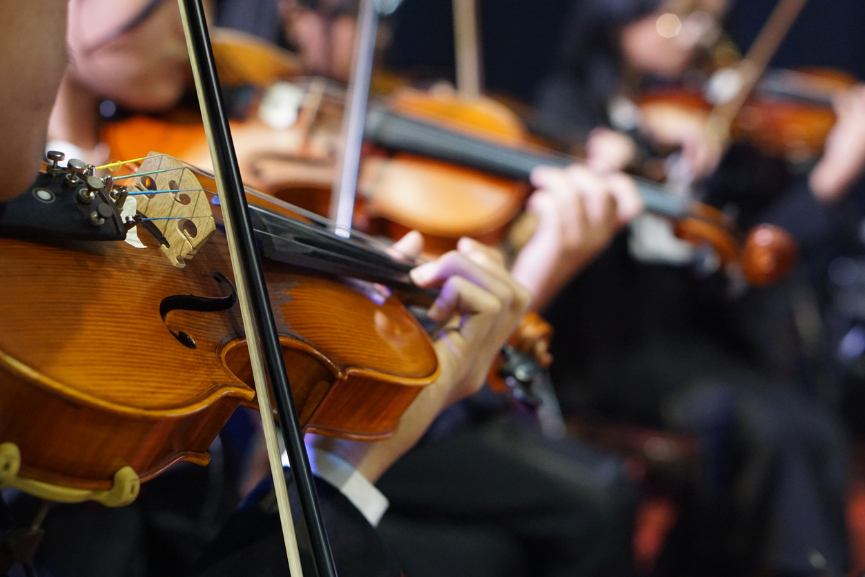 close up of hands playing violin in orchestra