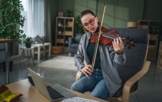 female adult violin learner playing in front of laptop