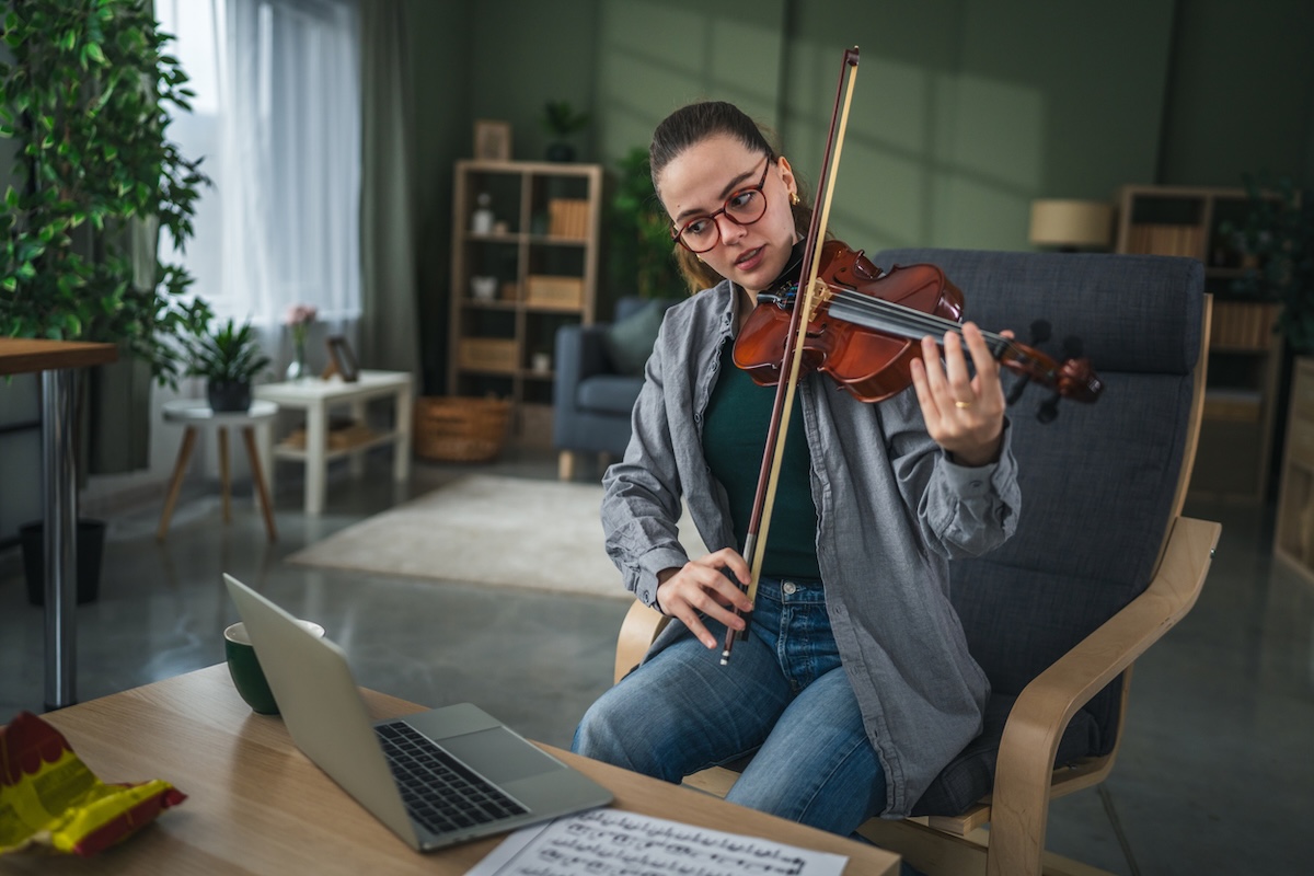 female adult violin learner playing in front of laptop