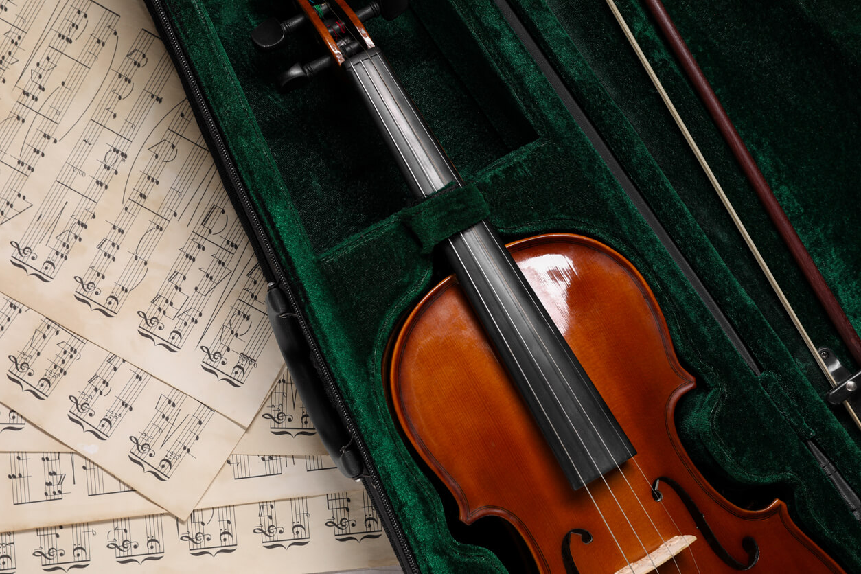 violin in a green velvet-lined case with sheet music underneath the case